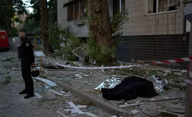 A policeman stands next to the bodies of two people killed during an overnight Russian attack in Kyiv, Ukraine, Thursday, Aug. 20, 2026. (AP Photo/Francisco Seco)