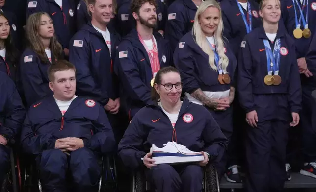 President Donald Trump speaks as alpine monoskier Laurie Stephens, front center, smiles, during an event for Olympic athletes, coaches, staff, and representatives from Team USA in the East Room of the White House, Thursday, Aug. 6, 2026, in Washington. (AP Photo/Alex Brandon)