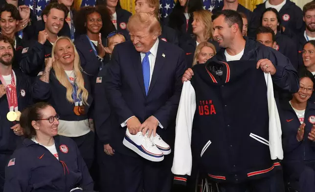 President Donald Trump poses with alpine monoskier Laurie Stephens, left, and bobsledder Frank Del Duca, right, who presented him with gifts, during an event for Olympic winter athletes, coaches, staff, and representatives from Team USA in the East Room of the White House, Thursday, Aug. 6, 2026, in Washington. (AP Photo/Alex Brandon)