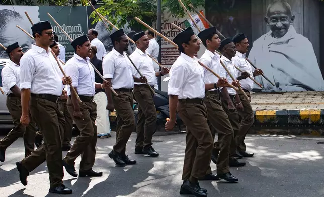 FILE - Rashtriya Swayamsevak Sangh (RSS) volunteers march through a street in Kochi, Kerala, India, Sunday, Oct. 13, 2024, in front of a poster of Mahatma Gandhi displayed as part of celebrations marking 100th year of Gandhi assuming office as the Indian National Congress party president. (AP Photo/R S Iyer, File)