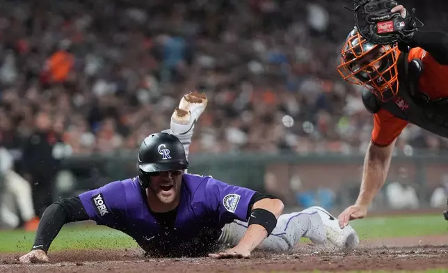 Colorado Rockies' Brett Sullivan, left, scores past San Francisco Giants catcher Andrew Knizner, right, during the fifth inning of a baseball game, Friday, Aug. 14, 2026, in San Francisco. (AP Photo/Jeff Chiu)