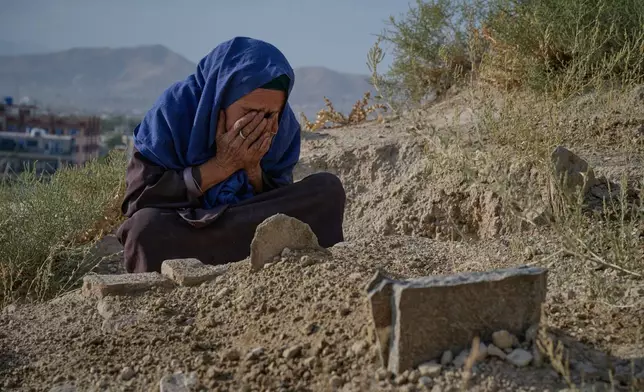 Sima covers her face at the grave of her six-month-old granddaughter, her daughter Diba's daughter, who died during the winter, in Kabul, Afghanistan, Wednesday, Aug. 12, 2026. Originally from Mazar-e-Sharif in northern Afghanistan, Sima, who believes she is about 60 but does not know her exact age, helps support her extended family by begging and collecting items she can reuse or sell. (AP Photo/Nava Jamshidi)