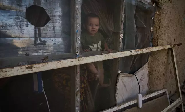 A child looks out the window of the room where Sima lives with several members of her extended family in Kabul, Afghanistan, Wednesday, Aug. 12, 2026. (AP Photo/Nava Jamshidi)