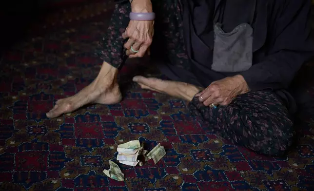 Sima sits beside money she collected while begging outside a mosque in Kabul, Afghanistan, Friday, Aug. 14, 2026. Although begging is prohibited, Sima said Taliban police allowed her to beg and even gave her some change as an exception during celebrations marking five years of Taliban rule. (AP Photo/Nava Jamshidi)