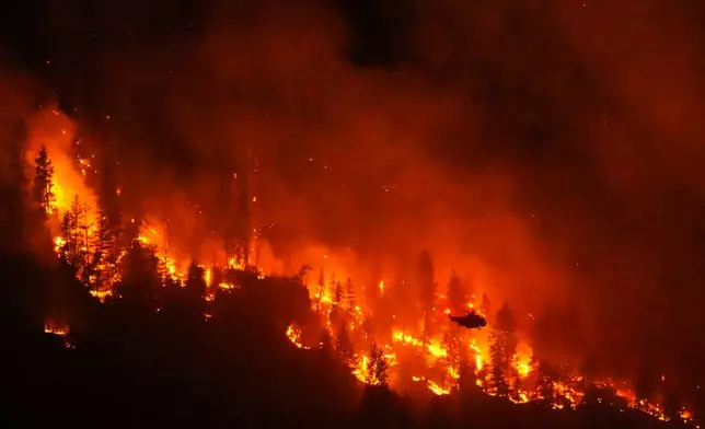 FILE - A helicopter conducting night operations prepares to drop water on the Quilpituk Creek wildfire burning on the west side of Okanagan Lake near Fintry, British Columbia, Aug. 3, 2026. (Darryl Dyck/The Canadian Press via AP, File)