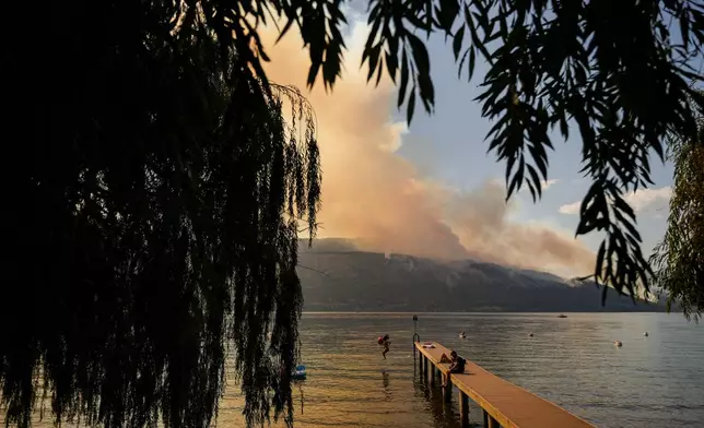 FILE - A woman jumps off a dock into Okanagan Lake, in Lake Country, British Columbia, as the Quilpituk Creek wildfire burns on the mountainside across the lake near Fintry, Aug. 3, 2026. (Darryl Dyck/The Canadian Press via AP, File)