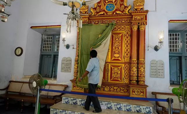 Synagogue trustee M.C. Praveen removes the ornate ceremonial curtain from the carved teakwood Torah ark, located on the western wall facing Jerusalem, at the 458-year-old Paradesi Synagogue in the historic Jew Town neighborhood of Kochi, India, Wednesday, May 20, 2026. (AP Photo/Aijaz Rahi)