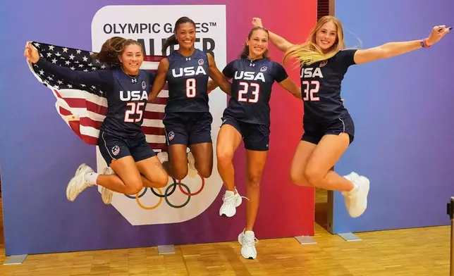 Loryn Goodwin, Ashlea Klam, Laneah Bryan and Isabella Geraci of the USA women's team jump with a United States flag during the media day ahead of the Flag Football World Championships, the sports first Olympic qualifier for LA28, in Duesseldorf, Germany, Wednesday, Aug. 12, 2026. (AP Photo/Martin Meissner)