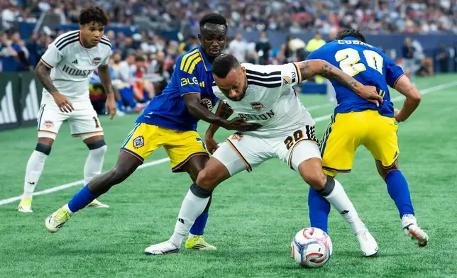 Houston Dynamo FC's Guilherme Santos, center, Vancouver Whitecaps' Cheick Sabaly, left, and Andres Cubas, right, vie for the ball during the first half of an MLS soccer match in Vancouver, B.C., on Wednesday, Aug. 19, 2026. (Ethan Cairns/The Canadian Press via AP)