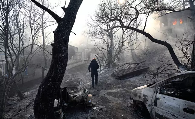 A firefighter walks through a burned area as flames engulf a house during a wildfire on the island of Salamina, west of Athens, Greece, Sunday, Aug. 16, 2026. (AP Photo/Michael Varaklas)