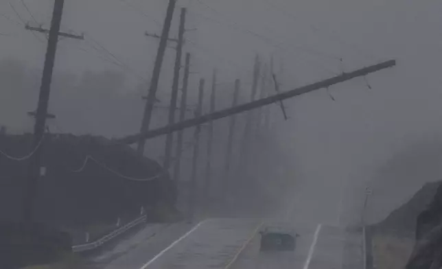A vehicle drives near a downed utility pole dangling above Mamalahoa Highway during Hurricane Lala near Ocean View, Hawaii, Saturday, Aug. 15, 2026. (Stephen Lam/San Francisco Chronicle via AP)