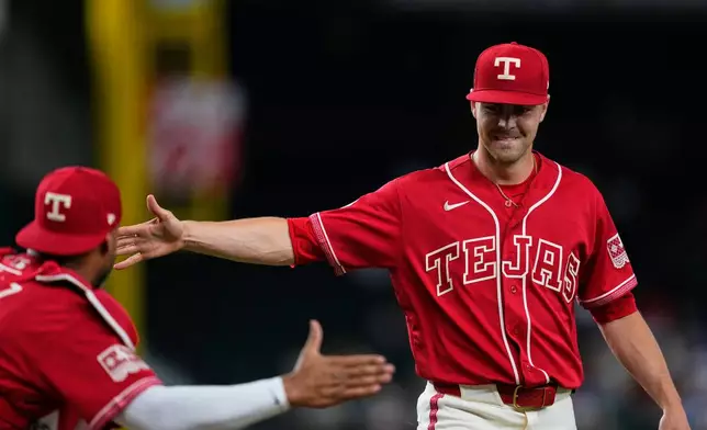 Texas Rangers' Elias Díaz, left, and MacKenzie Gore, right, celebrate after winning a pitch challenge in the first inning of a baseball game against the Los Angeles Angels Friday, Aug. 21, 2026, in Arlington, Texas. (AP Photo/Tony Gutierrez)
