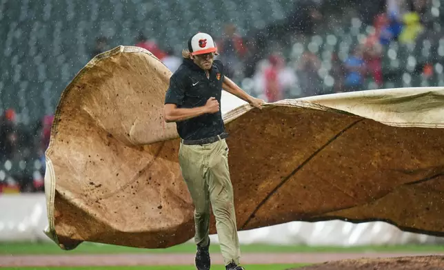 A member of the grounds crew places a tarp over the mound as a baseball game between the Baltimore Orioles and the Philadelphia Phillies is delayed for the second time due to rain, Sunday, Aug. 2, 2026, in Baltimore. (AP Photo/Stephanie Scarbrough)