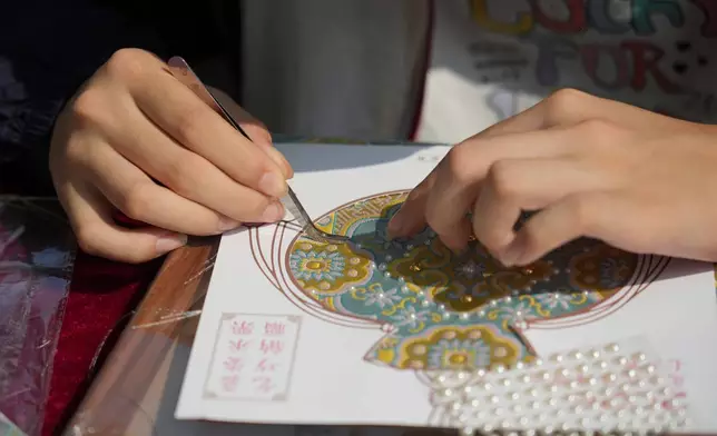 A child makes a sachet-shaped Song brocade pearl painting during a festival to celebrate Qixi at the Beijing Folk Custom Museum in Beijing, Wednesday, Aug. 19, 2026. (AP Photo/Achmad Ibrahim)