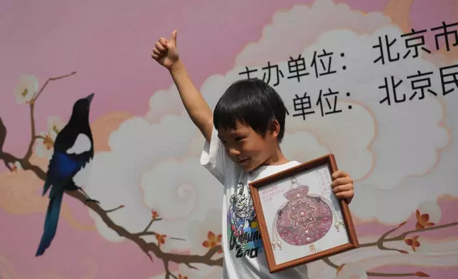 A child celebrates with his finished sachet-shaped Song brocade pearl painting during a festival to celebrate Qixi at the Beijing Folk Custom Museum in Beijing, Wednesday, Aug. 19, 2026. (AP Photo/Achmad Ibrahim)