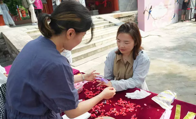 A woman gets her nail dyed with garden balsam, a natural pigment traditionally associated with beauty and blessings, during a festival to celebrate Qixi at the Beijing Folk Custom Museum in Beijing, Wednesday, Aug. 19, 2026. (AP Photo/Achmad Ibrahim)