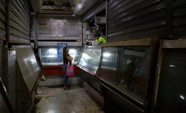 A woman shops at a butcher shop that remains open amid shuttered businesses in Caracas, Venezuela, Tuesday, Aug. 25, 2026. (AP Photo/Pedro Mattey)