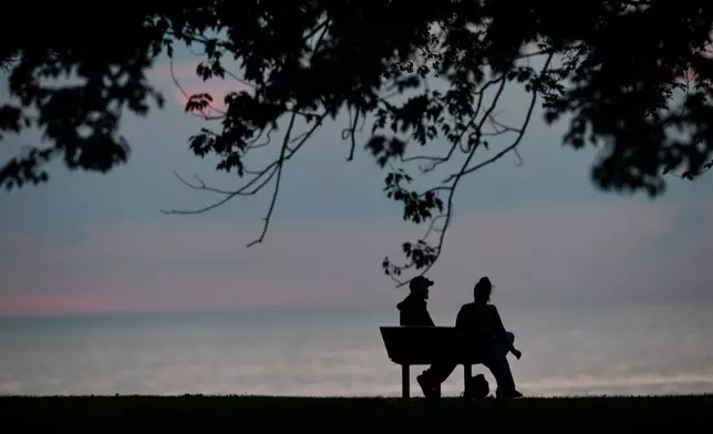 People watch the sun set over Lake Ontario, Tuesday, Aug. 25, 2026, in Olcott, N.Y. (AP Photo/Adrian Kraus)