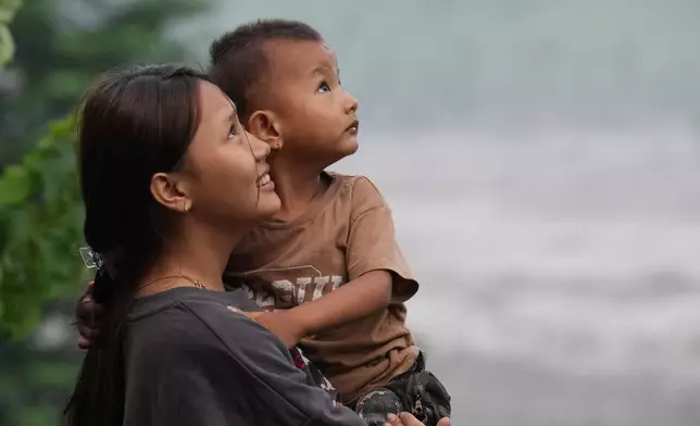 A girl holds a child as they watch a rescue helicopter fly by in Trishuli Bazaar area of Nuwakot district, Nepal, Sunday, Aug. 30, 2026. (AP Photo/Rajesh Kumar Singh)