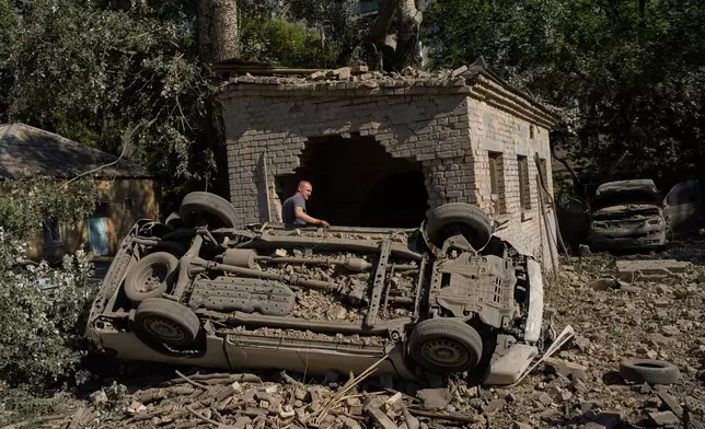 A local resident stands next to destroyed cars after an overnight Russian missiles and drones attack, in Kyiv, Ukraine, Thursday, Aug. 20, 2026 (AP Photo/Francisco Seco)