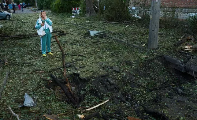 A woman stands next to a crater left during an overnight Russian attack, in Kyiv, Ukraine, Thursday, Aug. 20, 2026. (AP Photo/Francisco Seco)