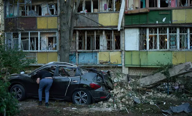 A local resident looks inside a destroyed car next to heavily damaged residential buildings after an overnight Russian attack, in Kyiv, Ukraine, Thursday, Aug. 20, 2026. (AP Photo/Francisco Seco)