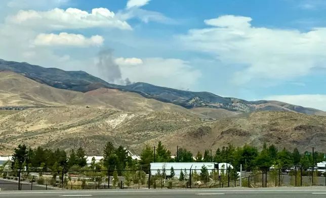 Smoke billows in the distance as a wildfire in Reno, Nev., destroyed homes and caused thousands to evacuate their homes, Sunday, August 23, 2026. (AP Photo/Haven Daley)