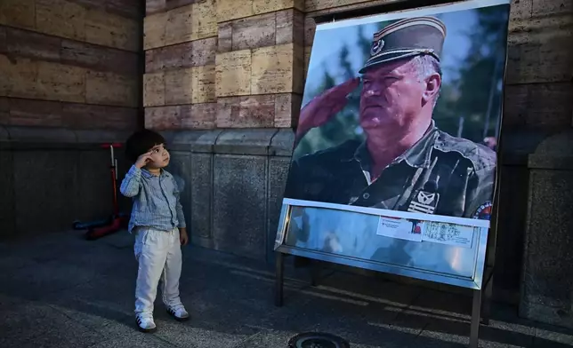 A boy salutes in front of poster of former Bosnian Serb wartime general Ratko Mladic, outside a church in Banja Luka, Bosnia-Herzegovina, Thursday, Aug. 27, 2026. (AP Photo/Radivoje Pavicic)