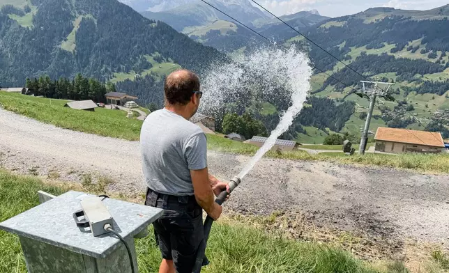 Juerg Klopfenstein, responsible for snowmaking operations at Adelboden-Lenk ski Resort, waters a road alongside ski slopes in Lenk valley near Adelboden, Switzerland, Monday, Aug. 3, 2026. (AP Photo/Hernan Munoz)