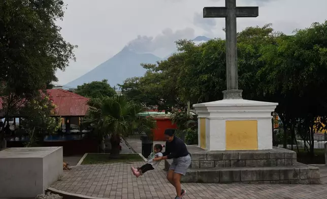 A woman playfully swings a child as clouds of ash rise from the crater of the Fuego volcano, as seen from San Pedro Las Huertas, Guatemala, Tuesday, Aug. 4, 2026. (AP Photo/Moises Castillo)