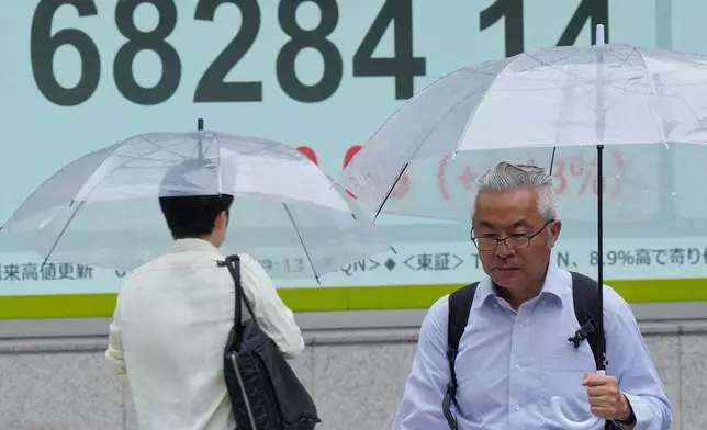 People walk in the rain near electronic stock board showing Japan's Nikkei index at a securities firm Thursday, Aug. 13, 2026, in Tokyo. (AP Photo/Eugene Hoshiko)