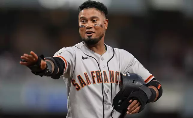 San Francisco Giants' Luis Arraez jokes with players in the San Diego Padres dugout as he stands on first base after getting hit by a pitch during the fourth inning of a baseball game Thursday, July 30, 2026, in San Diego. (AP Photo/Gregory Bull)