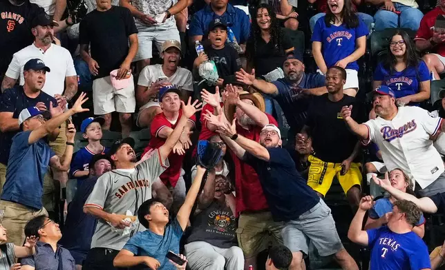 Fans compete for a San Francisco Giants' Jung Hoo Lee home run ball in the third inning of a baseball game against the Texas Rangers in Arlington, Texas, Monday, Aug. 3, 2026. (AP Photo/Tony Gutierrez)
