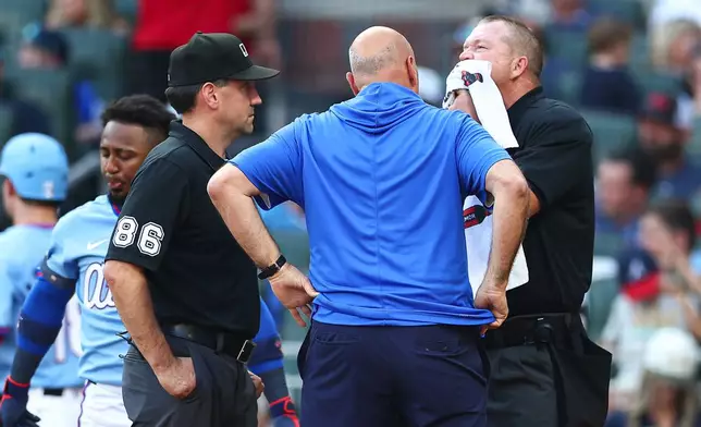 Home Plate umpire Ron Kulpa, right, gets evaluated by Braves trainer George Poulis, center, in the seventh inning of a baseball game between the Colorado Rockies and the Atlanta Braves, Saturday, Aug. 29, 2026, in Atlanta. (AP Photo/Colin Hubbard)
