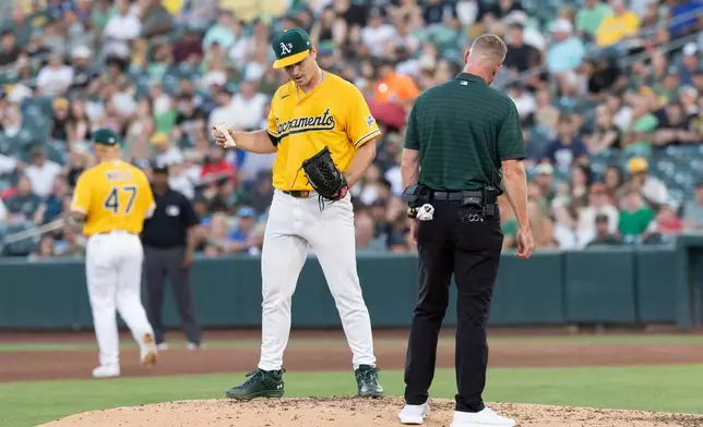 Athletics' trainer checks on pitcher J.T. Ginn, left, after catching a line drive hit by Texas Rangers' Brandon Nimmo during the 2-3 inning of a baseball game Saturday, Aug. 15, 2026, in West Sacramento, Calif. (AP Photo/Sara Nevis)