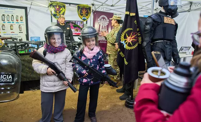 Juana Villano, right, and her sister Francesca pose for pictures at a police stand at a hunting, fishing and outdoors fair in Buenos Aires, Argentina, Friday, Aug. 14, 2026. (AP Photo/Rodrigo Abd)