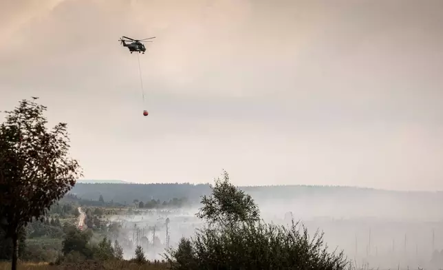 A helicopter prepares to dump a Bambi Bucket of water over a field as a wildfire burns near Waimes, Belgium, Monday, Aug. 17, 2026. (AP Photo/Valentin Bianchi)