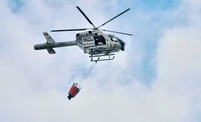 A police helicopter carries a Bambi Bucket as it prepares to drop water onto a wildfire buring in Waimes, Belgium, Monday, Aug. 17, 2026. (Photo AP/Marius Burgelman)