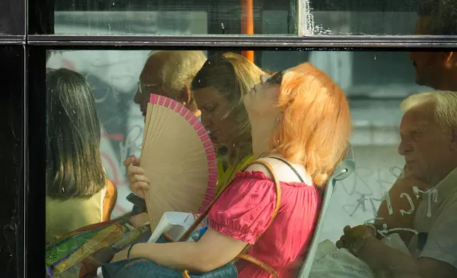 FILE - A woman uses a fan to cool off while riding a bus on a hot day in Bucharest, Romania, Aug. 6, 2026. (AP Photo/Vadim Ghirda)