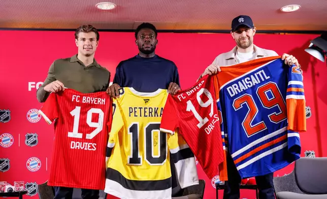 Boston Bruins’ John-Jason Peterka, from left, FC Bayern Munich’s Alphonso Davies, and Edmonton Oilers Leon Draisaitl, pose with jerseys during a joint press conference by FC Bayern Munich and the National Hockey League, Thursday, Aug. 20, 2026, in Munich. (Matthias Balk/dpa via AP)