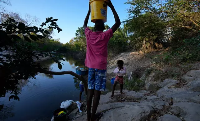 FILE - Children carry water from the Branco River at dawn at the Kalunga quilombo, a Brazilian settlement founded by escaped enslaved Africans, in the rural area of Cavalcante in Goias state, Brazil, Aug. 15, 2022. (AP Photo/Eraldo Peres, File)