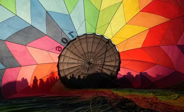 People's shadows are cast on a hot air balloon's envelope during the 5th edition of the Middle of the World International Hot Air Balloon Festival in Quito, Ecuador, Friday, Aug. 21, 2026. (AP Photo/Dolores Ochoa)