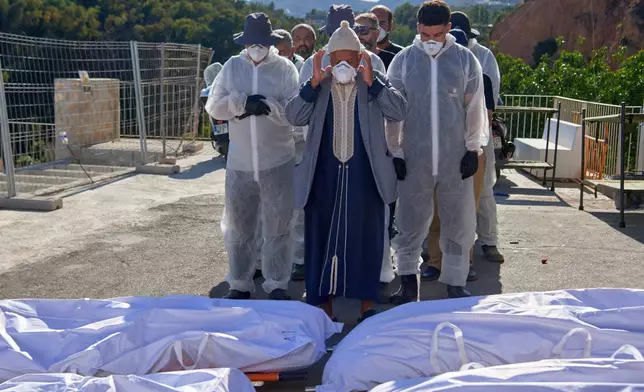A man, accompanied by funeral workers, prays over bodies of migrants who died while trying to cross from Morocco into the Spanish exclave of Ceuta, Friday, Aug. 21, 2026. (AP Photo/Antonio Sempere)