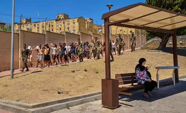 A Ceuta resident sits at a bus station as migrants who crossed into Spain are escorted by Spanish soldiers toward the Spanish-Moroccan border, for their return to Morocco from the Spanish enclave of Ceuta, Sunday, Aug. 2, 2026. (AP Photo/Bernat Armangue)