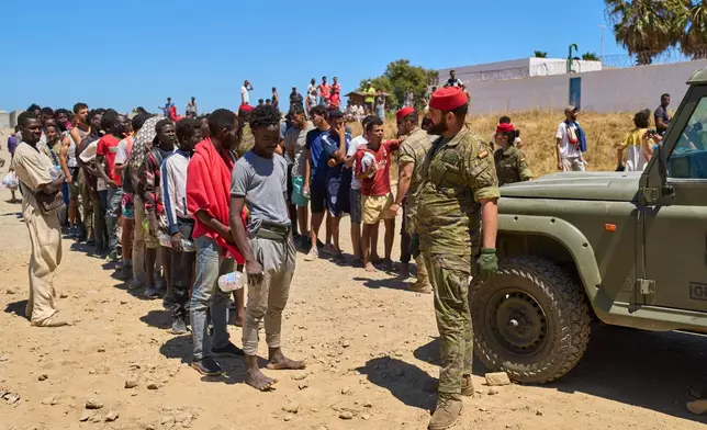 Migrants who crossed into Spain from Morocco line up for water distributed by Spanish soldiers in the Spanish enclave of Ceuta, Sunday, Aug. 2, 2026. (AP Photo/Bernat Armangue)