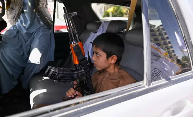 A boy holds an AK-style rifle while sitting in a vehicle decorated with Taliban flags during celebrations marking the fifth anniversary of the U.S. withdrawal from Afghanistan and the Taliban's return to power, in Kabul, Afghanistan, Saturday, Aug. 15, 2026. (AP Photo/Nava Jamshidi)