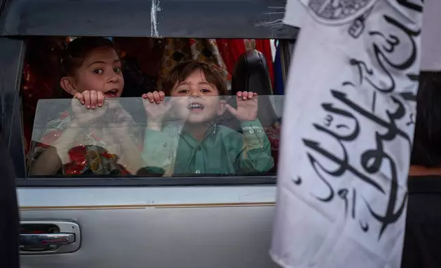 Young children look out from a car as a Taliban flag is held nearby on the eve of the fifth anniversary of the U.S. withdrawal and the start of Taliban rule in Kabul, Afghanistan, Friday, Aug. 14, 2026. (AP Photo/Nava Jamshidi)
