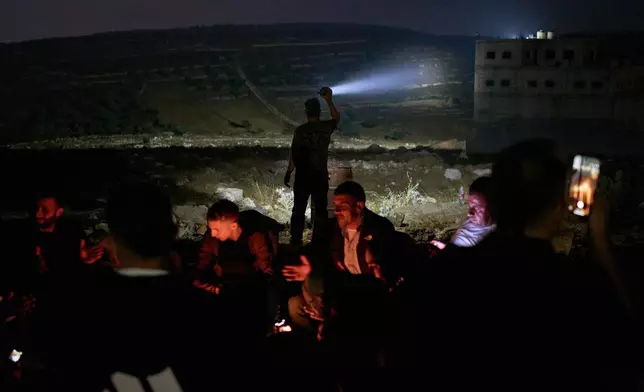 A Palestinian scans a valley with a flashlight as people gather around a bonfire during a volunteer night watch to help prevent Israeli settler attacks in the West Bank town of Sinjil, Monday, July 27, 2026. (AP Photo/Leo Correa)