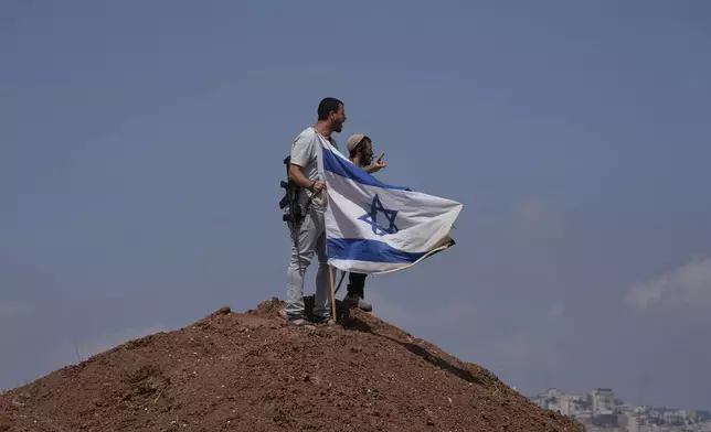 Israeli settlers put up an Israeli flag on a hilltop after it was taken down by Israeli and foreign peace activists during a protest in support of local landowners whose property is threatened with seizure by settlers, on the outskirts of the West Bank city of Beit Sahour, Friday, Aug. 14, 2026. (AP Photo/Mahmoud Illean)