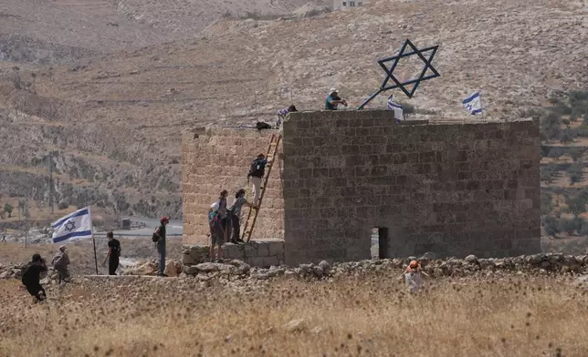 Israeli and foreign peace activists take down a metal structure in the shape of a Star of David from atop a Palestinian structure during a protest in support of local landowners whose property is threatened with seizure by Israeli settlers, on the outskirts of the West Bank city of Beit Sahour, Friday, Aug. 14, 2026. (AP Photo/Mahmoud Illean)